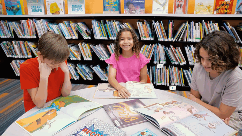 Kids read books together at a table in a library during an educational summer program in Orlando