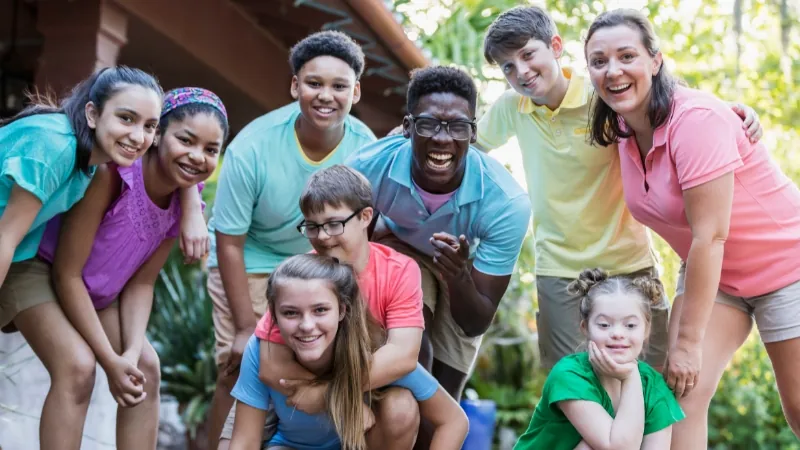 A group of smiling kids and camp counselors pose together outdoors at one of the inclusive summer camps in Orlando