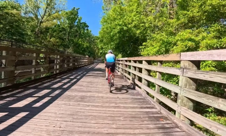 A person riding a bike across a wooden bridge surrounded by greenery