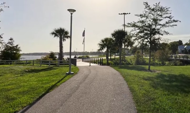 A serene pathway lined with trees and grass, leading to a tranquil body of water