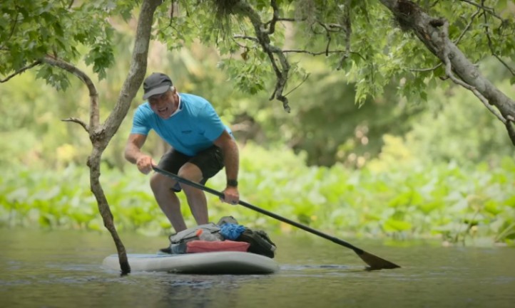 Man paddleboarding through dense, green foliage