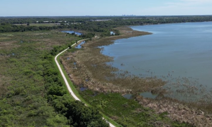 Aerial view of a serene lake bordered by a winding road, surrounded by lush greenery and natural landscape