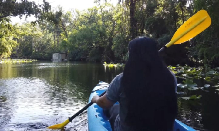 Person with long dark hair paddling a bright blue kayak with a neon yellow paddle
