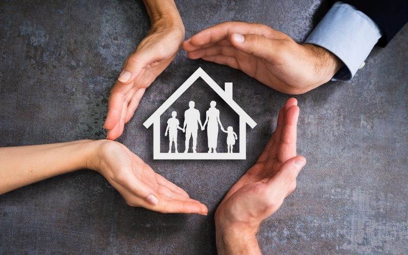 Hands surrounding a house symbol representing family protection and homeownership.