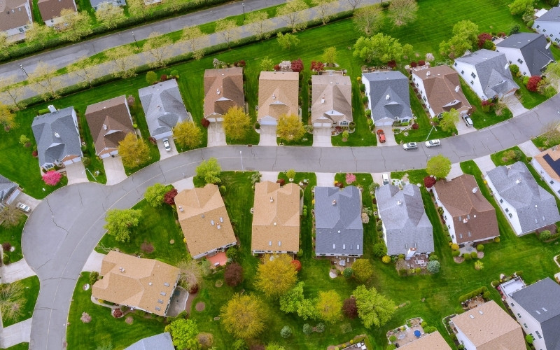 Aerial view of a suburban neighborhood with detached houses, green lawns, and residential streets.